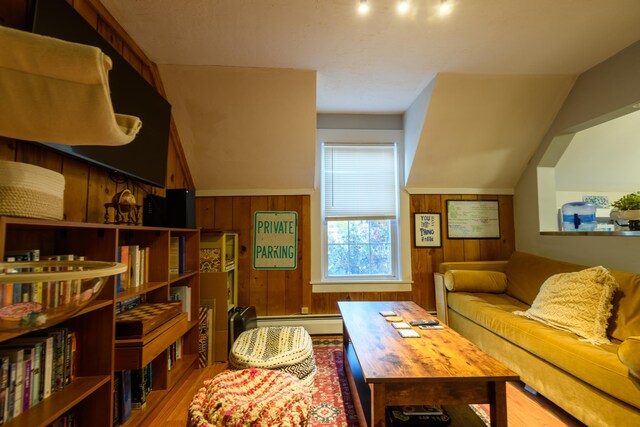 living room featuring lofted ceiling, wood walls, baseboard heating, and hardwood / wood-style flooring