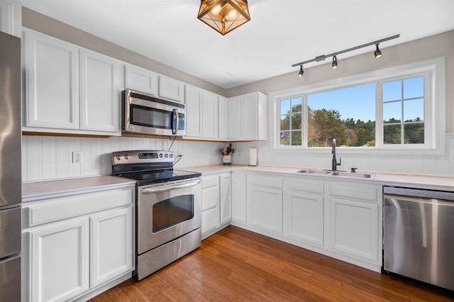 kitchen with rail lighting, stainless steel appliances, white cabinets, sink, and light hardwood / wood-style flooring