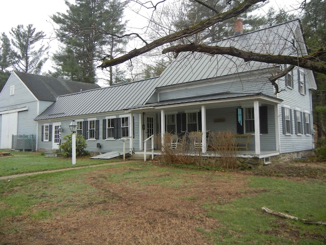 view of front of house with a porch, a front yard, metal roof, a chimney, and a standing seam roof