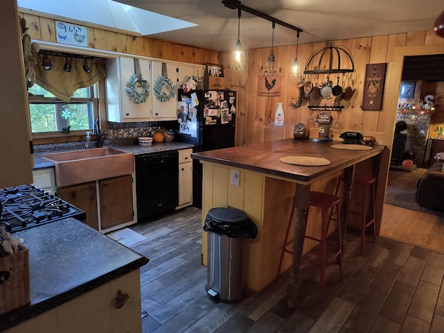 kitchen featuring a skylight, black appliances, dark hardwood / wood-style flooring, and wooden walls