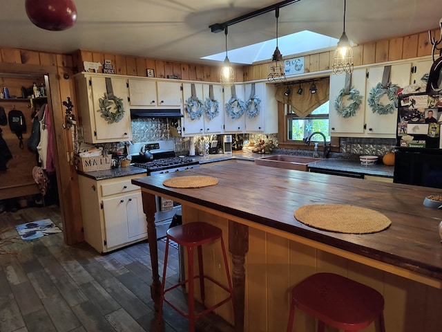 kitchen featuring a skylight, decorative light fixtures, sink, wood counters, and stainless steel range with gas stovetop