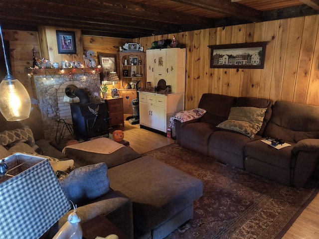 living room featuring beamed ceiling, light wood-type flooring, wood walls, and a wood stove