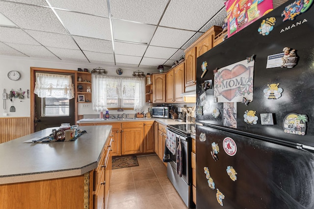 kitchen with wood walls, light tile patterned floors, a kitchen island, stainless steel appliances, and a drop ceiling