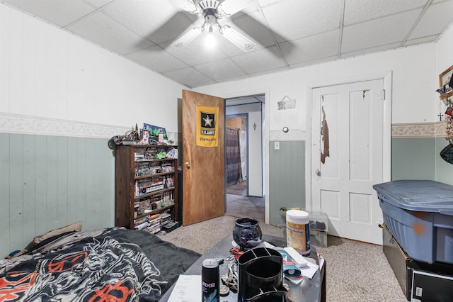 carpeted bedroom with a drop ceiling, wooden walls, and ceiling fan