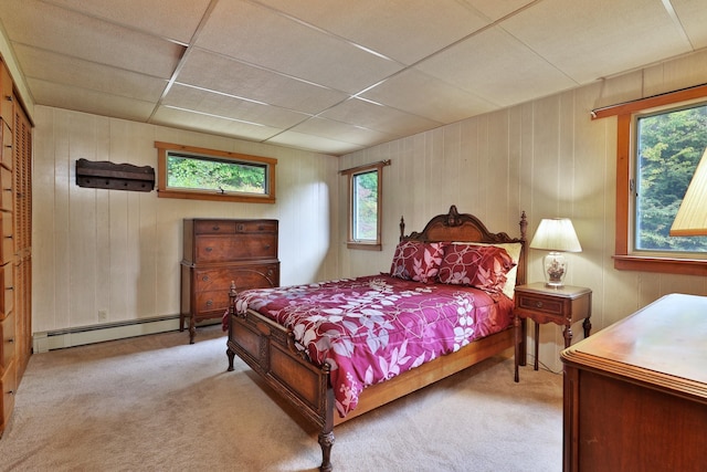 carpeted bedroom featuring a drop ceiling, wooden walls, and a baseboard radiator