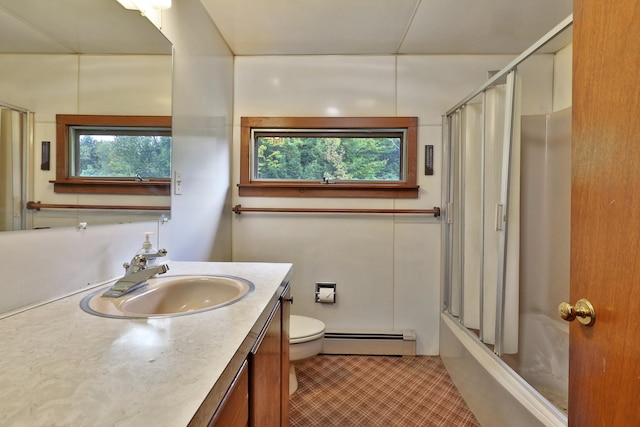 full bathroom with vanity, baseboard heating, combined bath / shower with glass door, tile patterned floors, and toilet