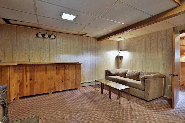 carpeted living room with a paneled ceiling, wood walls, and a baseboard heating unit