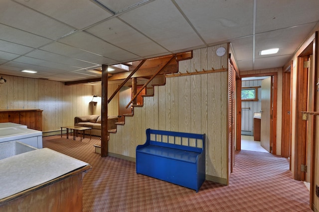 basement with carpet floors, a drop ceiling, and wood walls