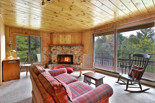 living room featuring wooden ceiling, wooden walls, a wealth of natural light, and a stone fireplace