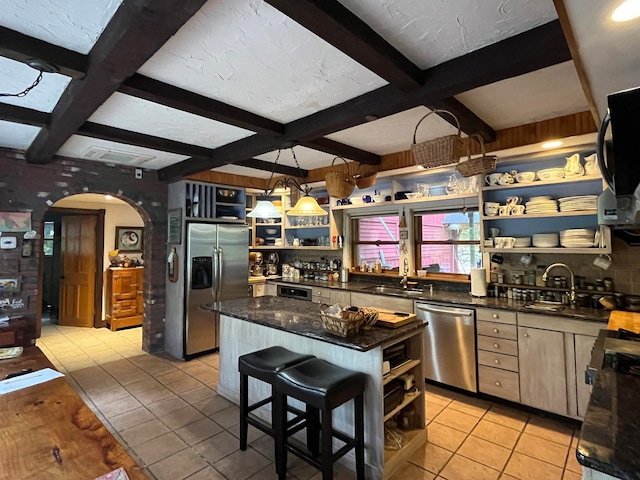 kitchen with appliances with stainless steel finishes, beam ceiling, a center island, and light tile patterned floors