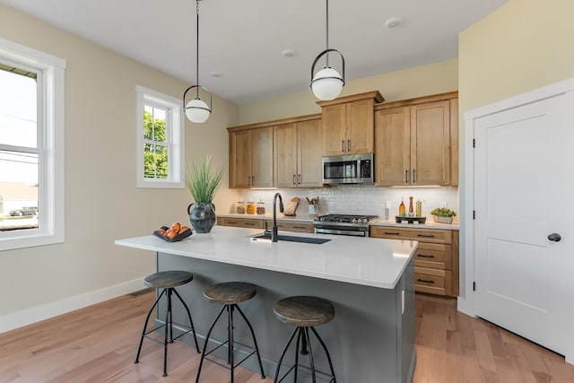 kitchen featuring light wood-type flooring, a kitchen island with sink, sink, hanging light fixtures, and appliances with stainless steel finishes