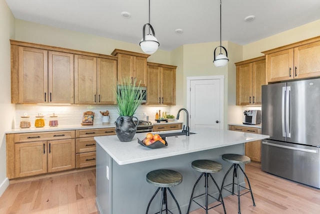 kitchen with a center island with sink, stainless steel appliances, hanging light fixtures, and light hardwood / wood-style floors