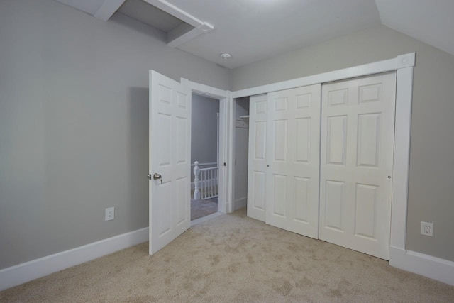 unfurnished bedroom featuring lofted ceiling, a closet, and light colored carpet