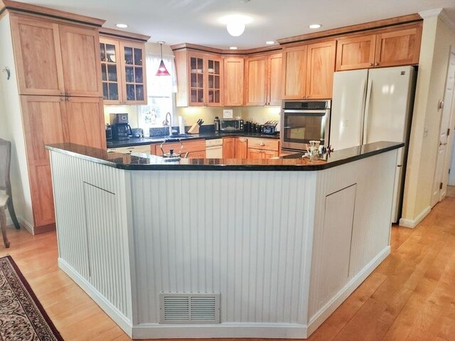 kitchen with hanging light fixtures, sink, white appliances, a kitchen island with sink, and light wood-type flooring