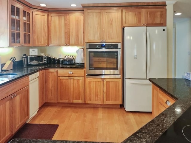 kitchen featuring dark stone countertops, light hardwood / wood-style flooring, and white appliances