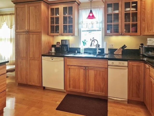 kitchen with dark stone countertops, sink, hanging light fixtures, light hardwood / wood-style flooring, and white dishwasher