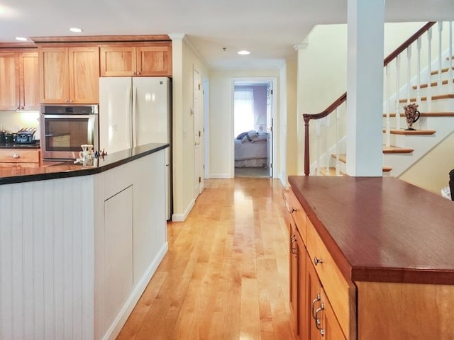 kitchen featuring white refrigerator, light hardwood / wood-style floors, crown molding, and stainless steel oven