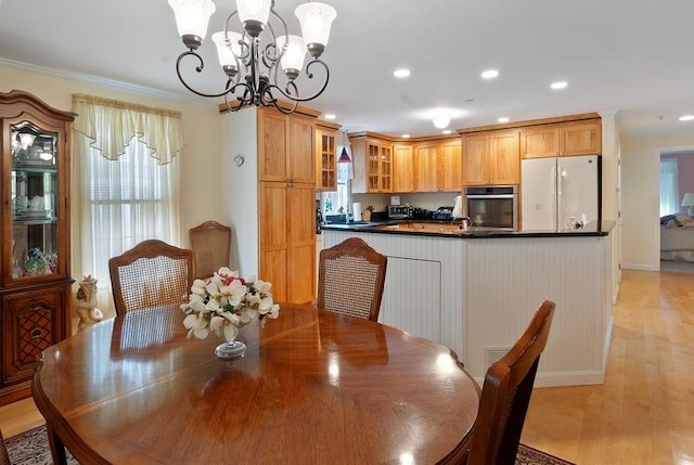 dining area with crown molding, an inviting chandelier, and light hardwood / wood-style flooring