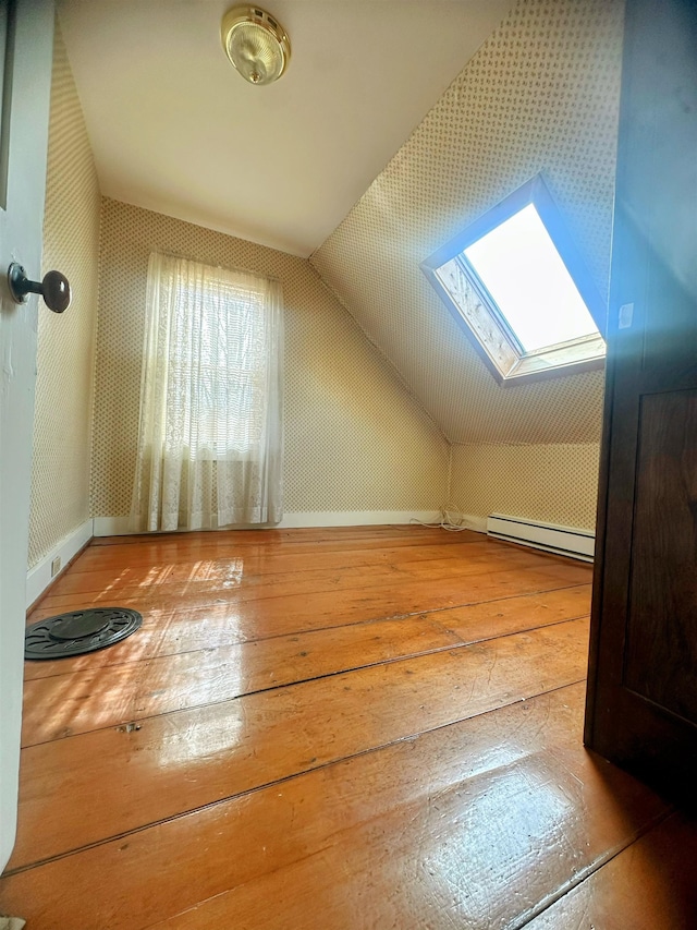 additional living space featuring wood-type flooring, a baseboard radiator, baseboards, and vaulted ceiling with skylight