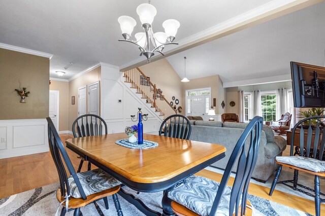 dining area with ornamental molding, a notable chandelier, lofted ceiling, and light hardwood / wood-style floors