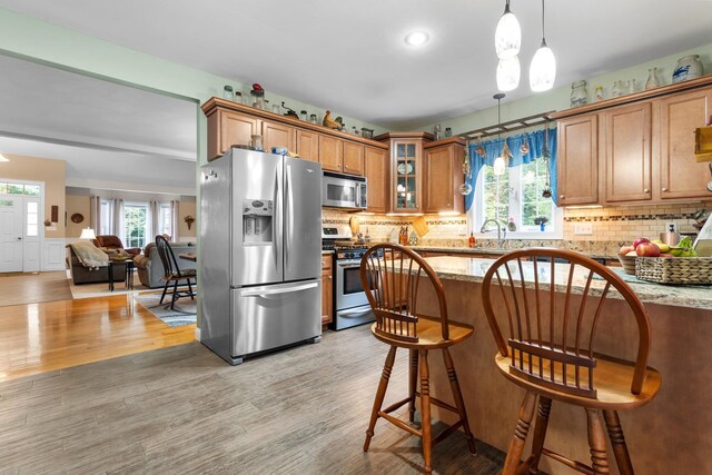 kitchen featuring appliances with stainless steel finishes, pendant lighting, light stone counters, and light hardwood / wood-style floors