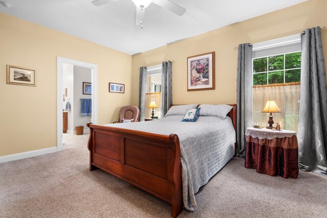 carpeted bedroom featuring connected bathroom, multiple windows, and ceiling fan