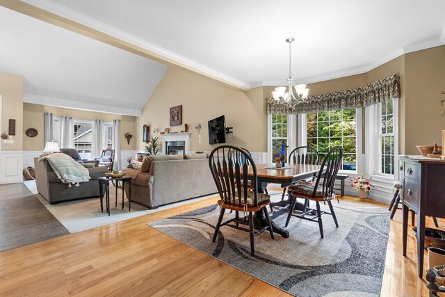 dining space featuring ornamental molding, light wood-type flooring, a notable chandelier, and lofted ceiling