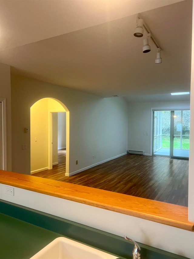 empty room with track lighting, a baseboard heating unit, and dark hardwood / wood-style floors