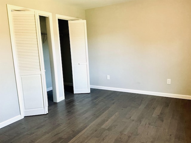 unfurnished bedroom with dark wood-type flooring, multiple closets, and baseboards