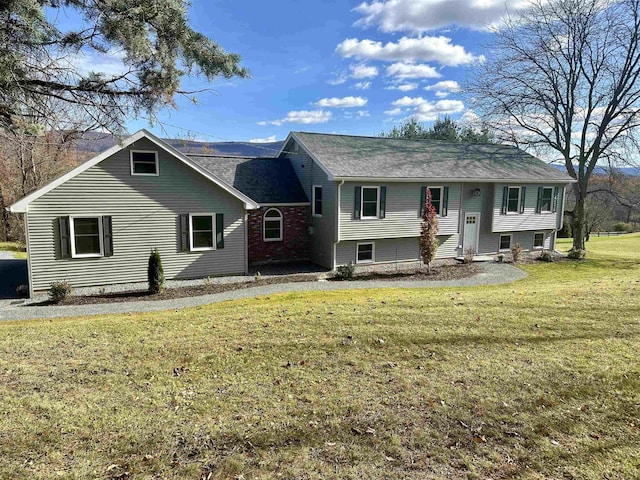 raised ranch featuring a shingled roof and a front lawn