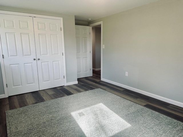 unfurnished bedroom with a closet, dark wood-style floors, and baseboards