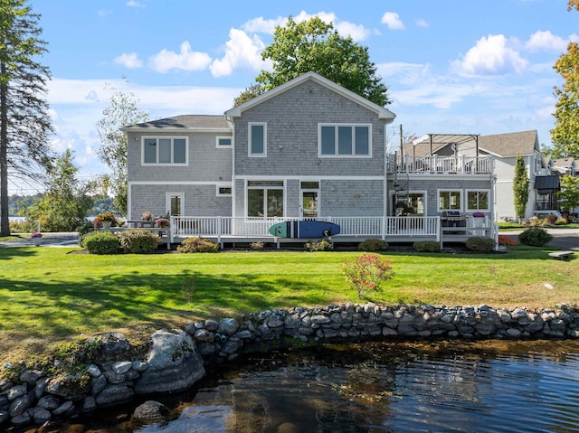 rear view of property featuring a lawn and a deck with water view