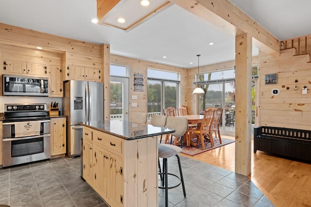 kitchen featuring dark wood-type flooring, dark stone counters, a kitchen bar, a kitchen island, and appliances with stainless steel finishes