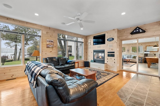 living room with ceiling fan, wood walls, and light wood-type flooring