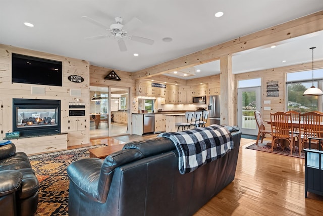 living room featuring wood walls, ceiling fan, light hardwood / wood-style floors, and a multi sided fireplace