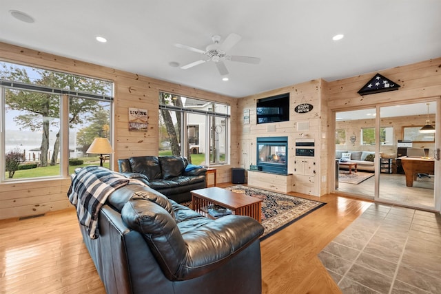 living room with wooden walls, plenty of natural light, ceiling fan, and light hardwood / wood-style flooring