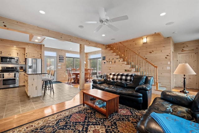 living room featuring light hardwood / wood-style flooring, ceiling fan, and wood walls