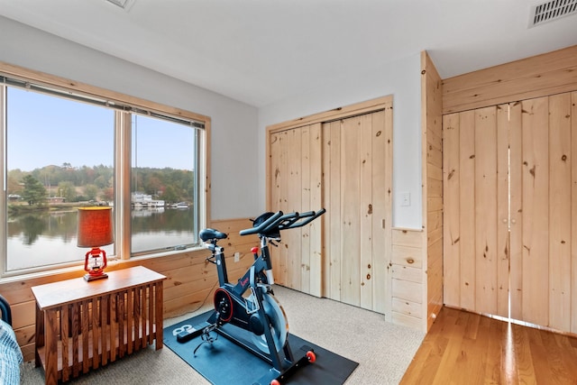 exercise area with wood walls, hardwood / wood-style floors, and a water view