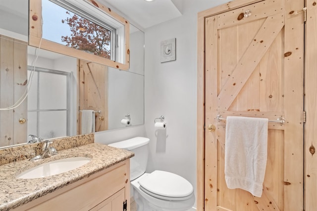 bathroom featuring vanity, a shower with shower door, and toilet