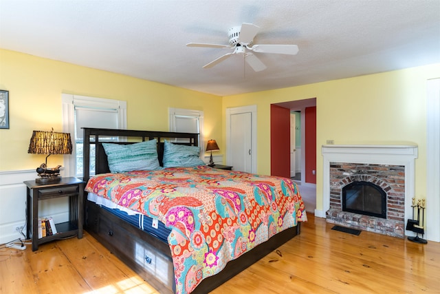 bedroom featuring ceiling fan, a textured ceiling, light wood-type flooring, and a fireplace