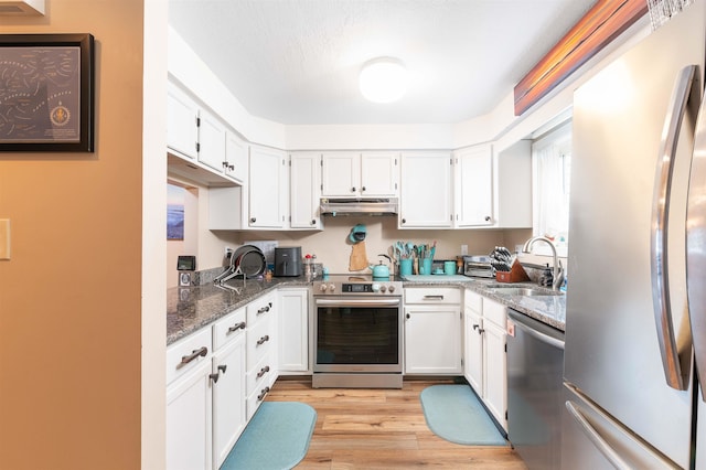 kitchen featuring light hardwood / wood-style flooring, dark stone counters, sink, white cabinets, and appliances with stainless steel finishes