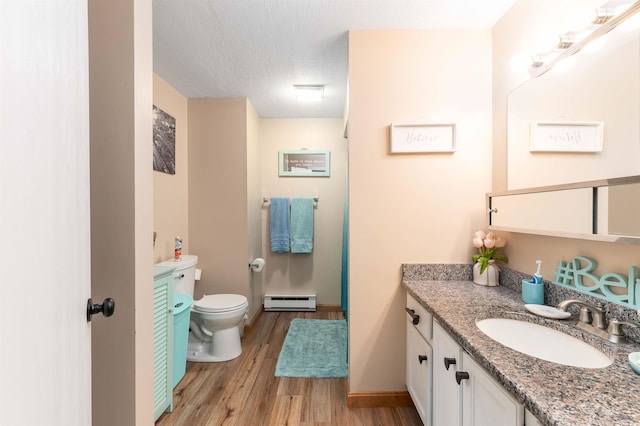 bathroom with a textured ceiling, hardwood / wood-style flooring, toilet, vanity, and baseboard heating