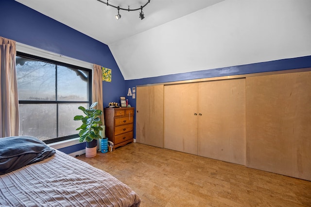 carpeted bedroom with a closet, rail lighting, and vaulted ceiling