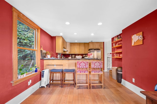 kitchen with kitchen peninsula, a kitchen bar, light wood-type flooring, and stainless steel refrigerator