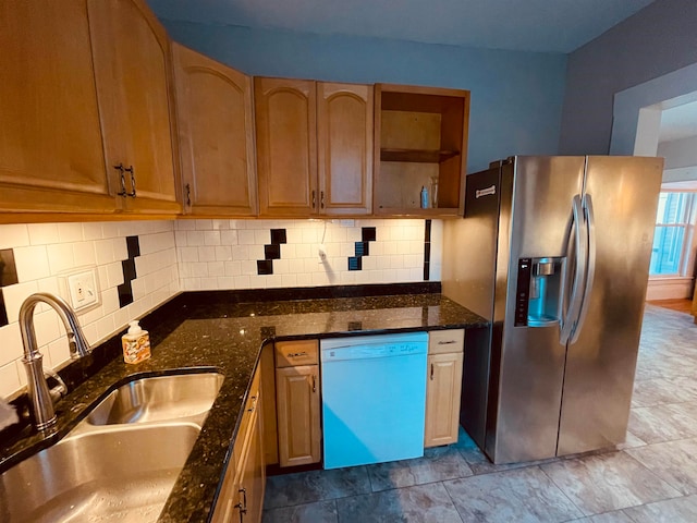 kitchen featuring stainless steel refrigerator with ice dispenser, dishwasher, dark stone countertops, and sink