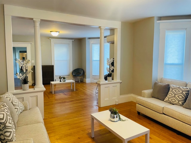 living room featuring ornate columns, light hardwood / wood-style flooring, a wall mounted AC, and radiator heating unit