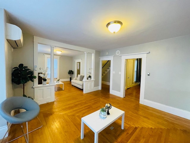 living room with decorative columns, light wood-type flooring, and a wall unit AC