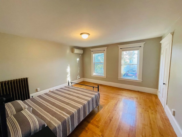 bedroom with light hardwood / wood-style floors, a wall mounted AC, and radiator heating unit