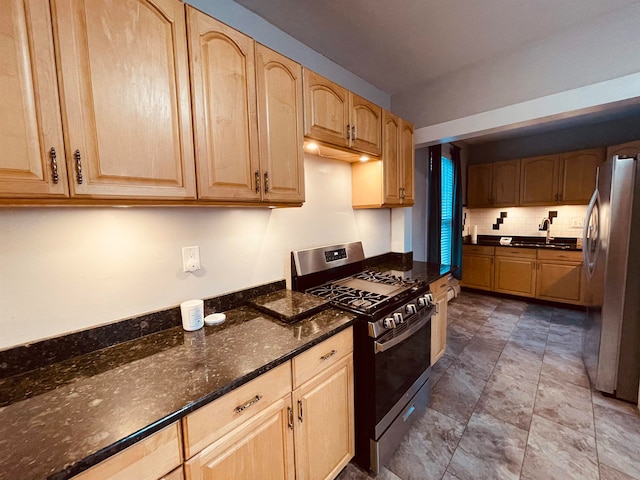 kitchen featuring appliances with stainless steel finishes, sink, light brown cabinetry, backsplash, and dark stone counters