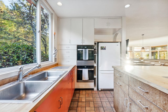 kitchen featuring white cabinets, hanging light fixtures, white refrigerator, sink, and stainless steel double oven